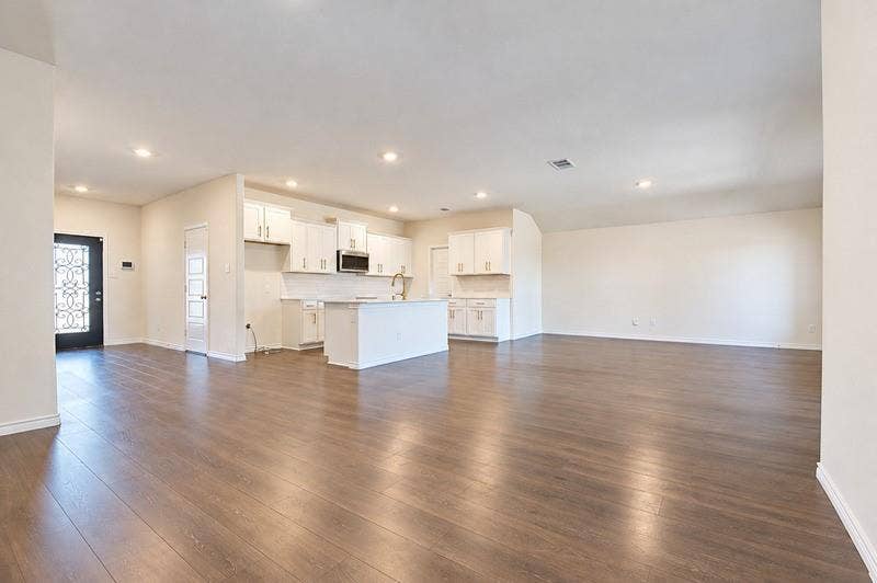 339 Exploration Way, Fate, TX 75189 Spacious open-concept living area with wood-finish flooring, recessed lighting, and a kitchen featuring white cabinetry, a central island, and a subway tile backsplash