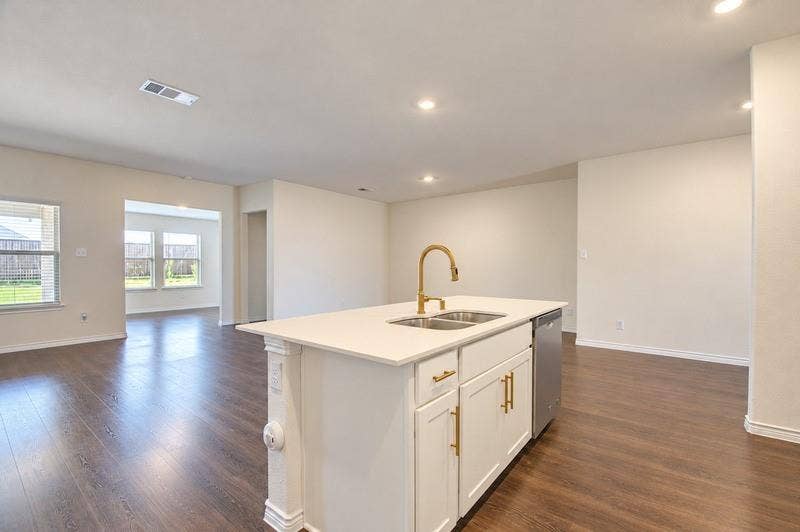 339 Exploration Way, Fate, TX 75189 Central island featuring a dual-basin sink with a gold-finish faucet, white cabinetry, and a light-toned countertop