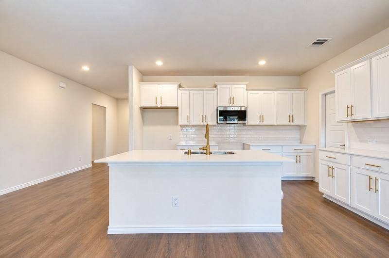 339 Exploration Way, Fate, TX 75189 Modern kitchen featuring white cabinetry, a large center island with a sink, stainless steel microwave, and wood-finish flooring
