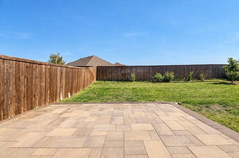 339 Exploration Way, Fate, TX 75189 Expansive paver patio with a contrasting border, leading to a lawn area with a wood privacy fence