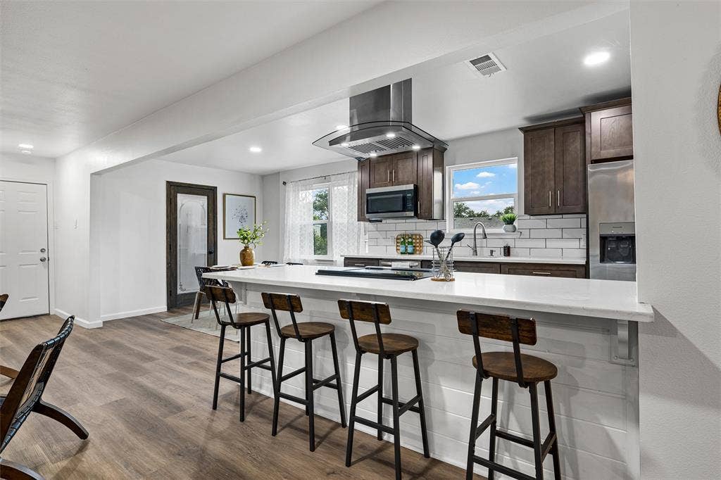 1132 Western Oaks Drive, Woodway, TX 76712 Kitchen featuring dark wood-finish cabinetry, stainless steel appliances, a subway tile backsplash, and a large central island with a white countertop