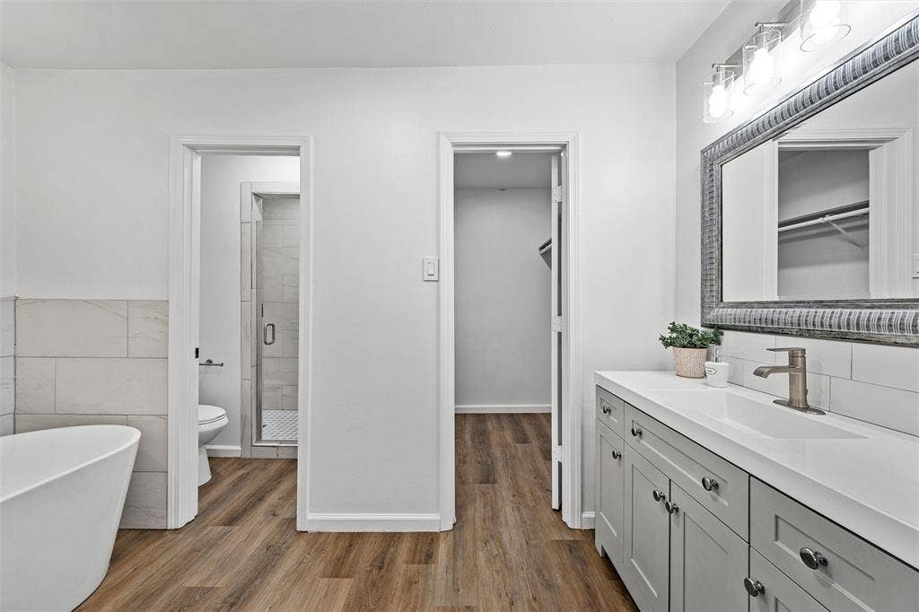 1132 Western Oaks Drive, Woodway, TX 76712 Bathroom featuring a freestanding tub, wood-finish flooring, a vanity with a white countertop, and a walk-in shower with a glass enclosure