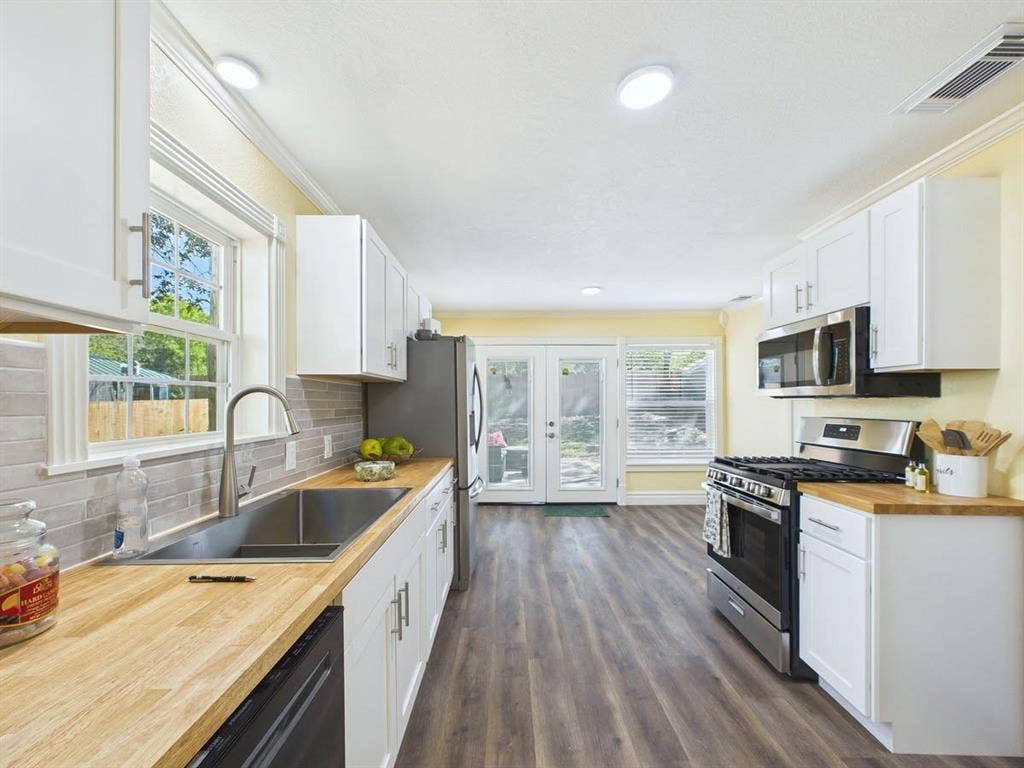 510 S Westmoreland Road, Dallas, TX 75211 Galley kitchen featuring wood-finish countertops, white cabinetry, stainless steel appliances, and wood-finish flooring