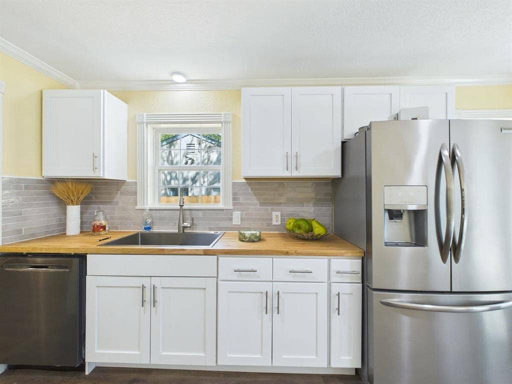510 S Westmoreland Road, Dallas, TX 75211 White shaker-style cabinetry with matte silver hardware, wood-finish countertops, stainless steel appliances, and a tile backsplash