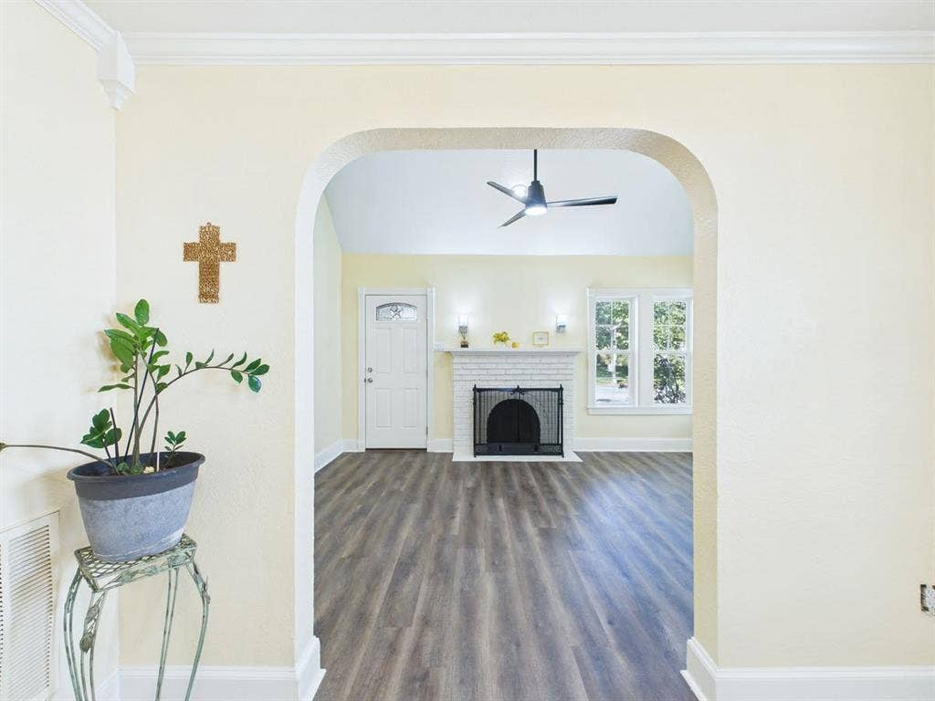 510 S Westmoreland Road, Dallas, TX 75211 Archway entry to a living space featuring wood-finish flooring, a white brick fireplace with a black screen, a white entry door with decorative glass, and a ceiling fan