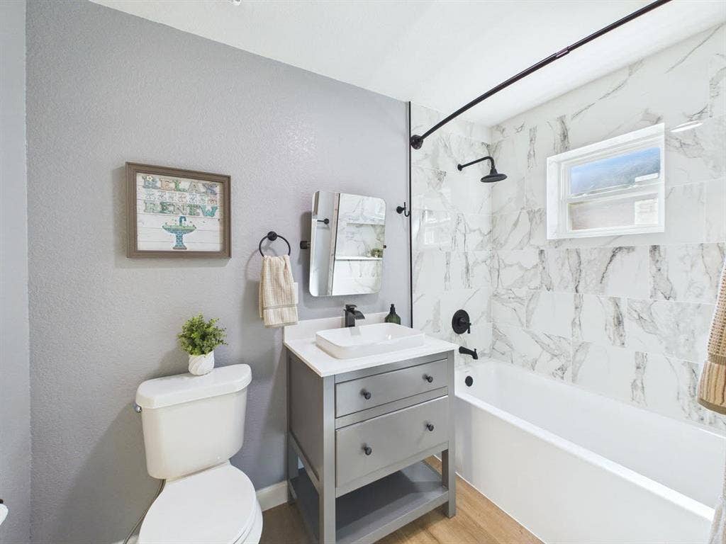510 S Westmoreland Road, Dallas, TX 75211 Wall-mounted shower head with matte black fixtures, white rectangular bathtub, wood-finish flooring, vanity with integrated vessel sink, and large format wall tile