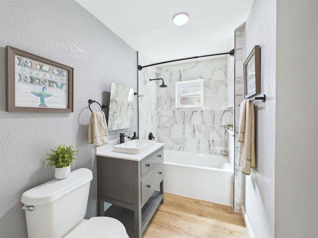 510 S Westmoreland Road, Dallas, TX 75211 Bathroom featuring a white bathtub, marble-look tile surround, dark gray vanity with a vessel sink, and wood-finish flooring
