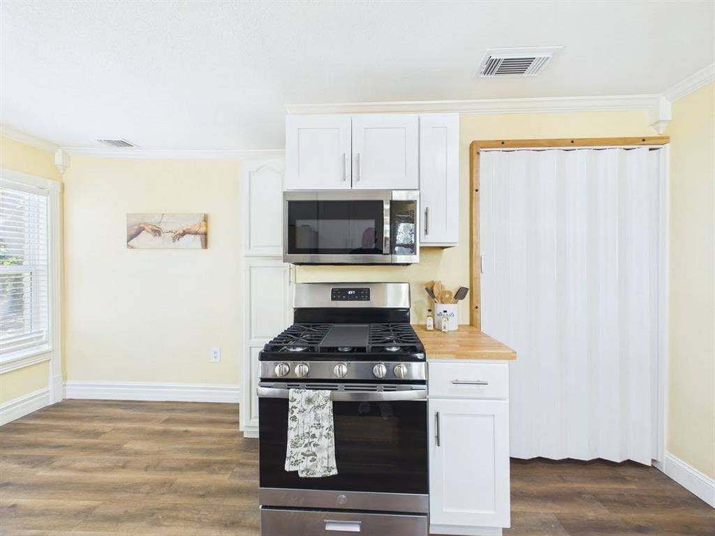 510 S Westmoreland Road, Dallas, TX 75211 Stainless steel range with an overhead microwave, white upper and lower cabinetry, wood-finish flooring, and crown molding