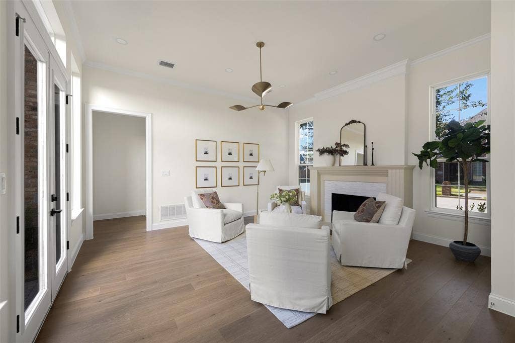 5901 Glen Heather Drive, Plano, TX 75093 Inviting front living room with a fireplace, warm wide-plank engineered wood flooring, contemporary ceiling fixture, and large windows bringing abundant light into the space.