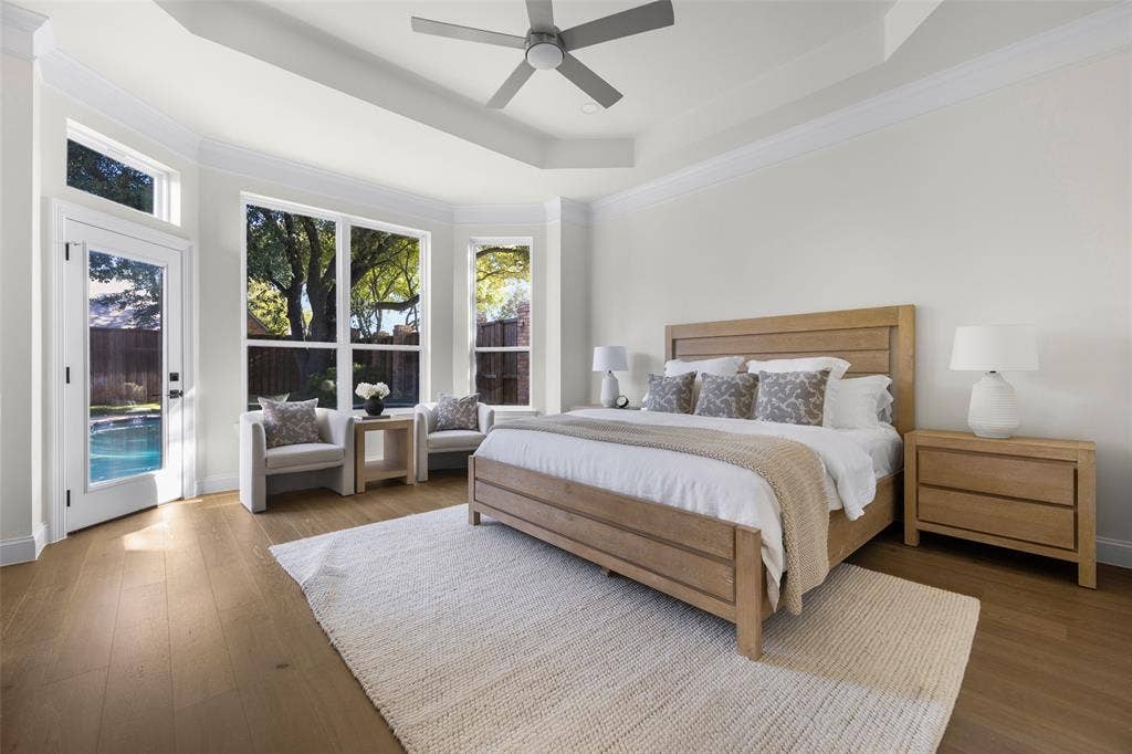 5901 Glen Heather Drive, Plano, TX 75093 Spacious first-floor primary suite features a tray ceiling, wide-plank wood flooring, contemporary ceiling fan, sitting area, and expansive windows overlooking the backyard and pool.