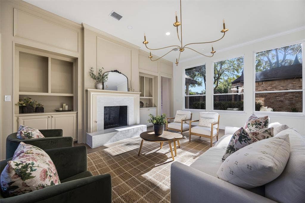 5901 Glen Heather Drive, Plano, TX 75093 Refined living room centered around a fireplace with extensive custom built-ins and detailed millwork, complemented by a sculptural chandelier and a wall of windows overlooking the backyard.