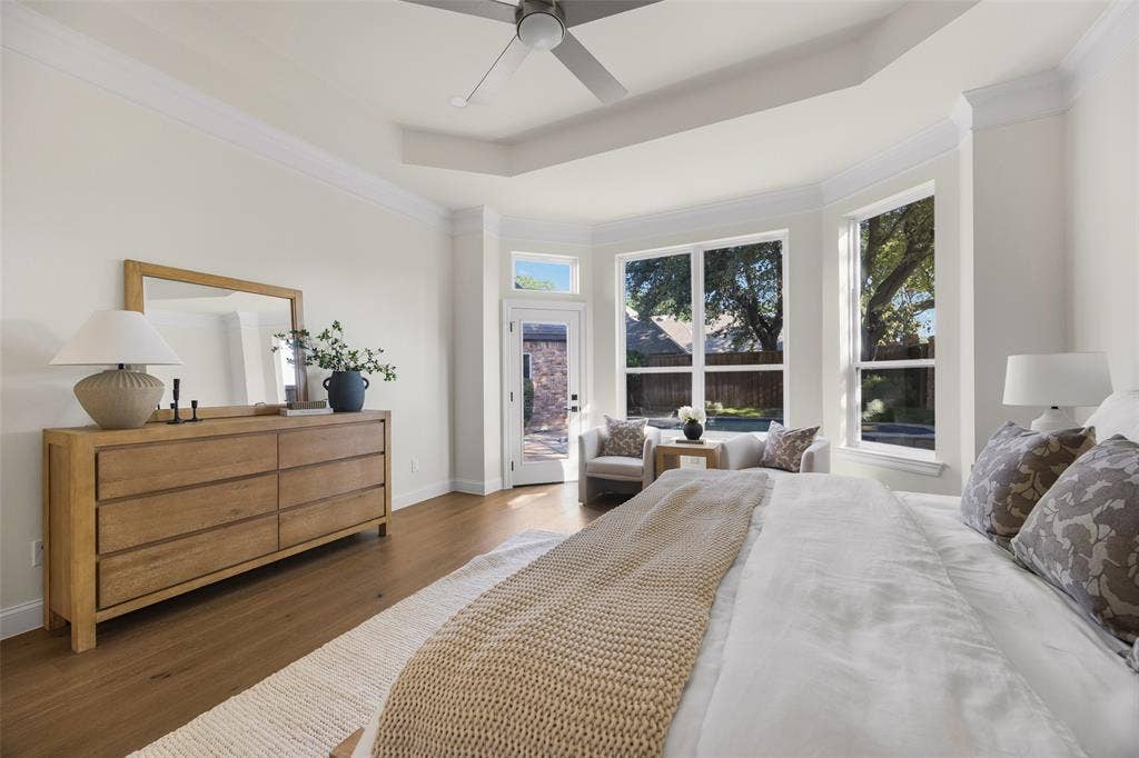 5901 Glen Heather Drive, Plano, TX 75093 Spacious first-floor primary suite features a tray ceiling, wide-plank wood flooring, contemporary ceiling fan, sitting area, and expansive windows overlooking the backyard and pool.