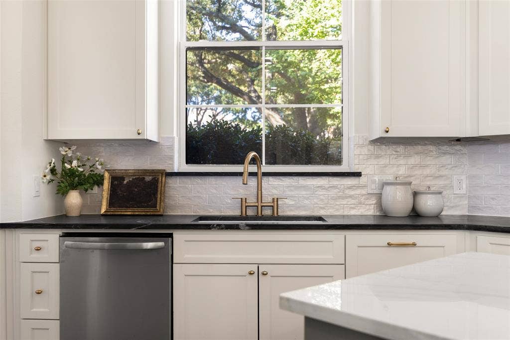 5901 Glen Heather Drive, Plano, TX 75093 Oversized kitchen window fills the workspace with natural light, highlighting the dark perimeter countertops, undermount sink, brass-toned faucet, stainless-steel dishwasher, and crisp cabinetry.