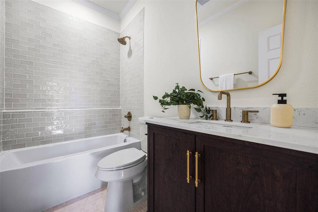 5901 Glen Heather Drive, Plano, TX 75093 Updated full bath pairs a dark wood vanity and quartz countertop with brass-toned fixtures, a softly framed mirror, and a tub-shower combination surrounded by tile.