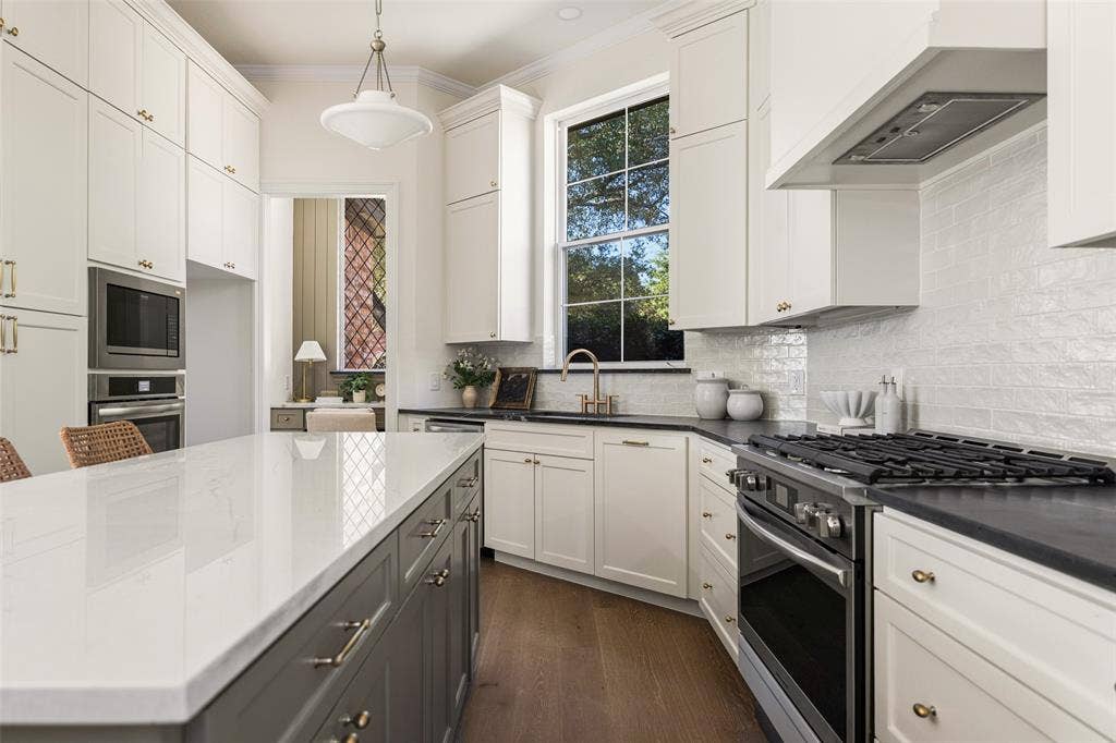 5901 Glen Heather Drive, Plano, TX 75093 Beautifully reimagined kitchen featuring two-tone cabinetry, quartz countertops, a 6-burner gas range, custom vent hood, statement backsplash, brass-toned hardware, and an oversized center island.