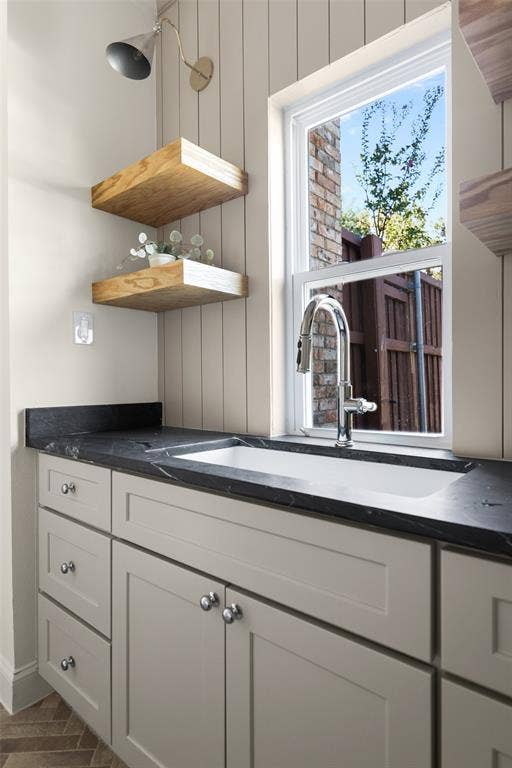 5901 Glen Heather Drive, Plano, TX 75093 Built-in utility sink is surrounded by generous cabinetry and dark countertop space, with floating wood shelves and a large window adding both practical storage and natural light to the laundry and mudroom area.
