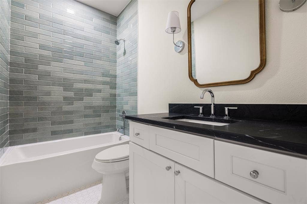 5901 Glen Heather Drive, Plano, TX 75093 Updated full bath features a tub and shower combination with floor-to-ceiling glazed tile, dark stone countertop, shaker-style cabinetry, and a decorative framed mirror.
