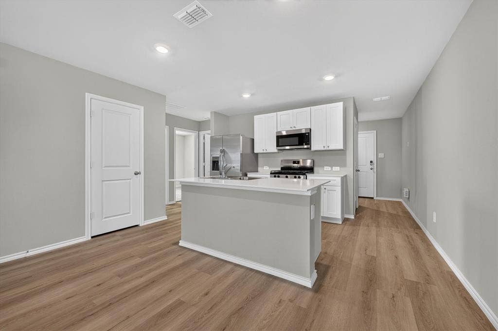 5413 Flannel Lane, Denton, TX 76249 Kitchen featuring an island with white countertop, white cabinetry, stainless steel appliances, and wood-finish flooring