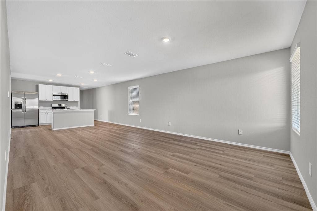 5413 Flannel Lane, Denton, TX 76249 Open-concept living space featuring wood-finish flooring, recessed lighting, and a kitchen with stainless steel appliances, white cabinetry, and a central island
