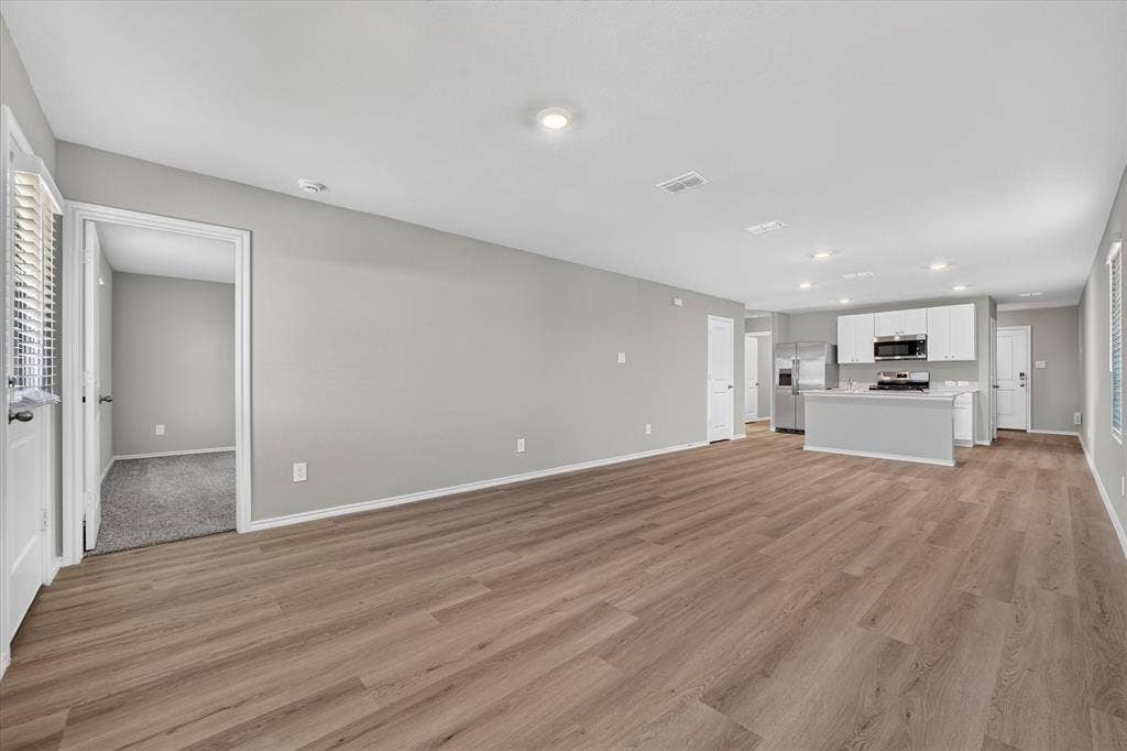 5413 Flannel Lane, Denton, TX 76249 Open-concept living space featuring wood-finish flooring, recessed lighting, and a kitchen with white cabinetry, stainless steel appliances, and a central island
