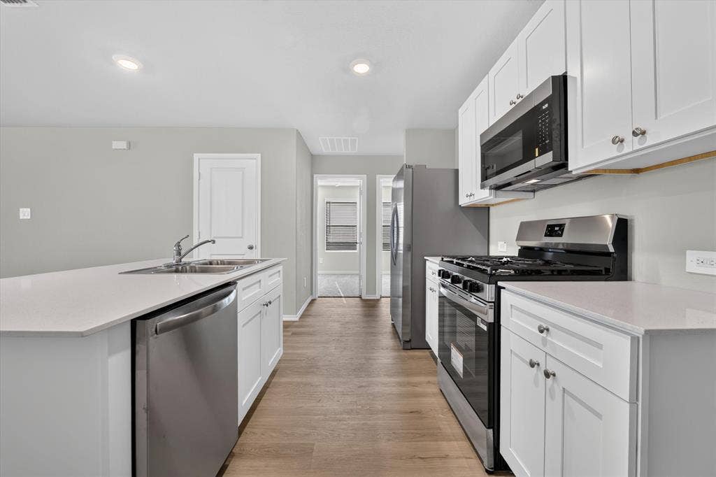 5413 Flannel Lane, Denton, TX 76249 Kitchen featuring an island with a double basin sink, white cabinetry, stainless steel appliances, wood-finish flooring, and recessed lighting