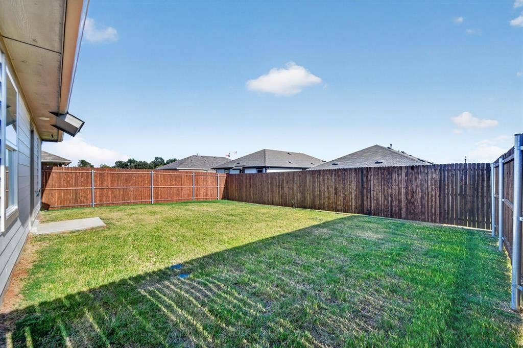 5413 Flannel Lane, Denton, TX 76249 Expansive fenced backyard with a manicured lawn, complete with a concrete pad and exterior wall lighting