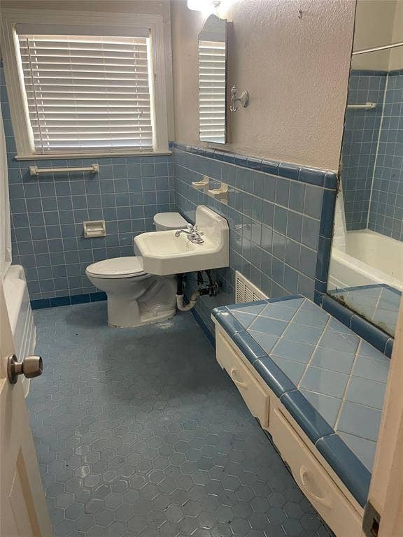 1527 Harbor Road, #1527, Dallas, TX 75216 Bathroom featuring light blue tiled walls, hexagonal floor tiling, a white wall-mounted sink, and a built-in storage bench with tiled top