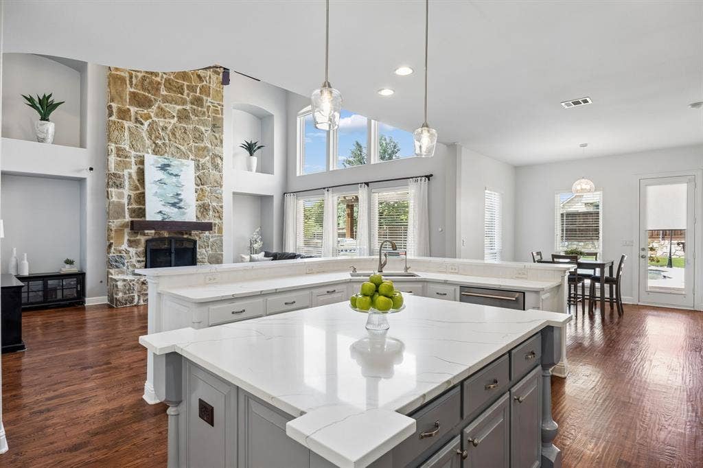 1011 Three Rivers Drive, Prosper, TX 75078 Stunning open-concept kitchen with expansiveisland, quartz countertops, and seamless connection to the light-filled living spaces, highlighted by soaring ceilings and a dramatic stone fireplace.
