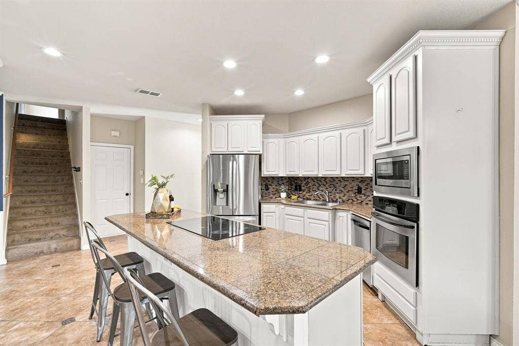 7030 Pecan Creek Circle, Midlothian, TX 76065 Chef-ready kitchen featuring white cabinetry, a center island with a cooktop, and granite counters.