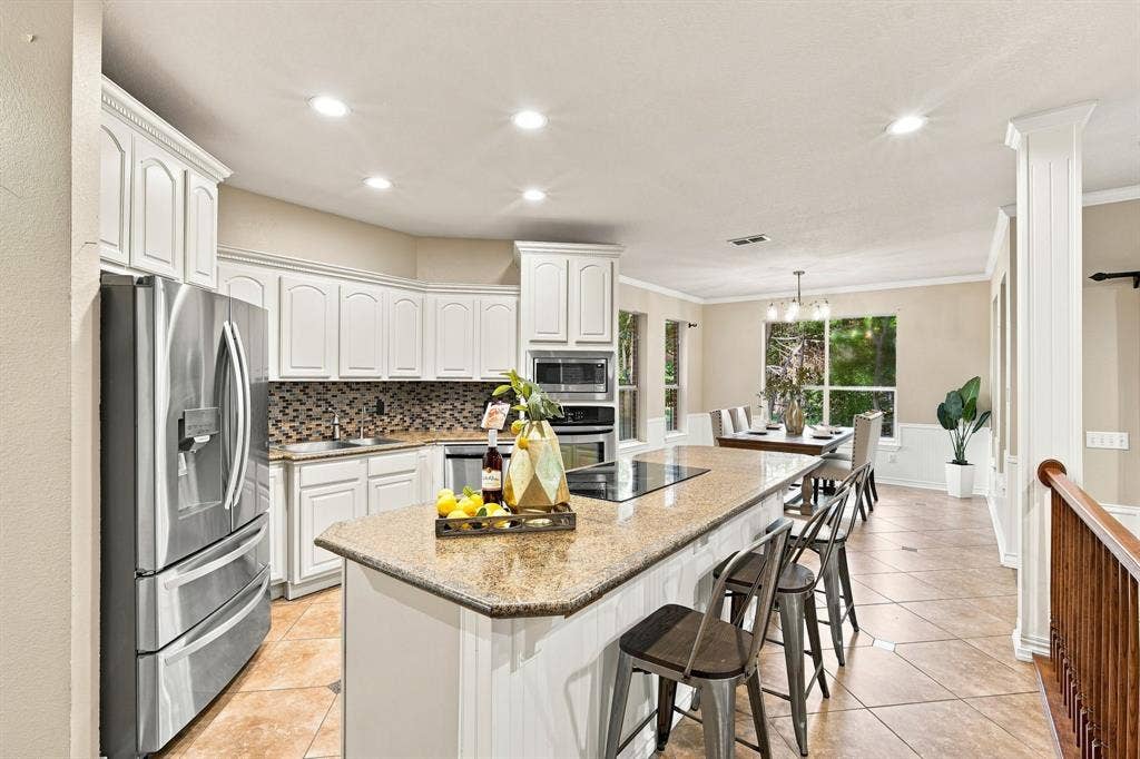 7030 Pecan Creek Circle, Midlothian, TX 76065 Beautifully appointed kitchen with crisp white cabinetry, a spacious island with a cooktop, and a stylish tile backsplash.
