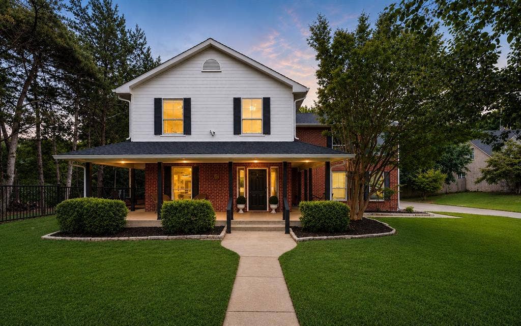 7030 Pecan Creek Circle, Midlothian, TX 76065 Picture-perfect curb appeal with a charming wraparound-style covered porch, mature trees, manicured landscaping, and a timeless brick-and-siding exterior.