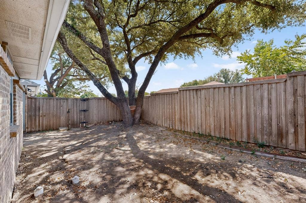 1606 Treehouse Lane, Plano, TX 75023 Private backyard space featuring a mature shade tree, a wood privacy fence, and a brick exterior wall