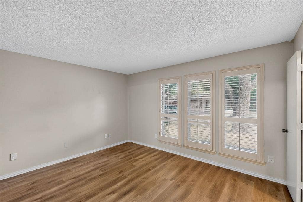 1606 Treehouse Lane, Plano, TX 75023 Wood-finish flooring, neutral wall paint, white trim, and three windows with plantation shutters
