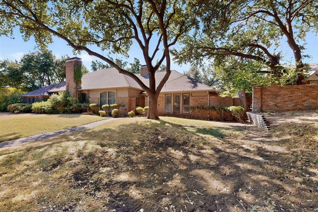 1606 Treehouse Lane, Plano, TX 75023 Brick exterior with a prominent chimney, mature trees, and a concrete walkway