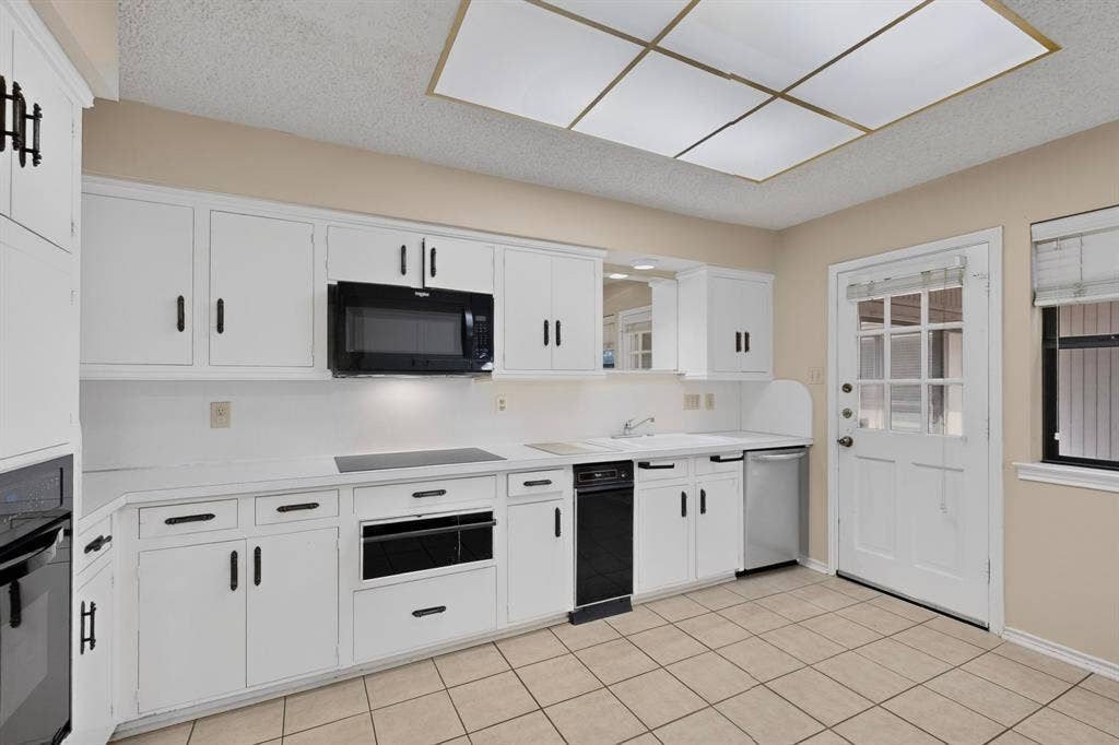 1606 Treehouse Lane, Plano, TX 75023 White cabinetry with matte black hardware, integrated black appliances, tiled flooring, built-in microwave, and a glass-paned exterior door