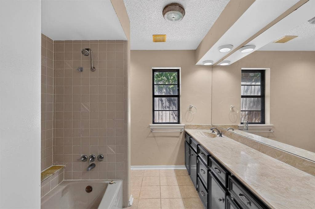 1606 Treehouse Lane, Plano, TX 75023 Full-length vanity mirror with overhead lighting, dual windows, and a combination tub-shower with tiled surround and built-in ledge