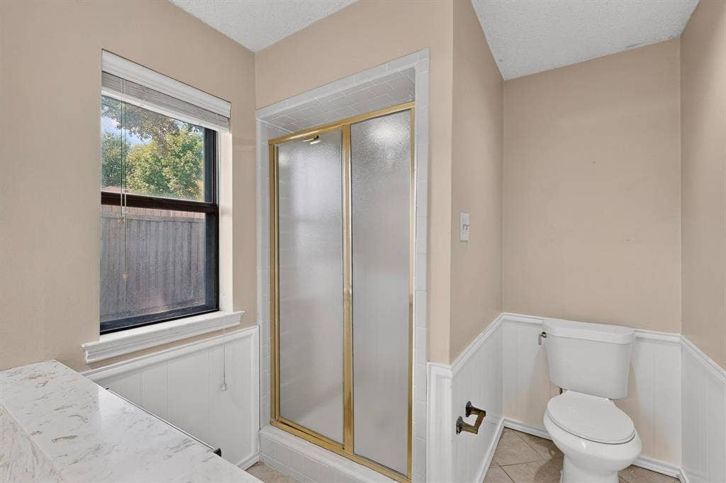 1606 Treehouse Lane, Plano, TX 75023 Shower with frosted glass doors and gold-tone framing, white wainscoting, and a window with blinds