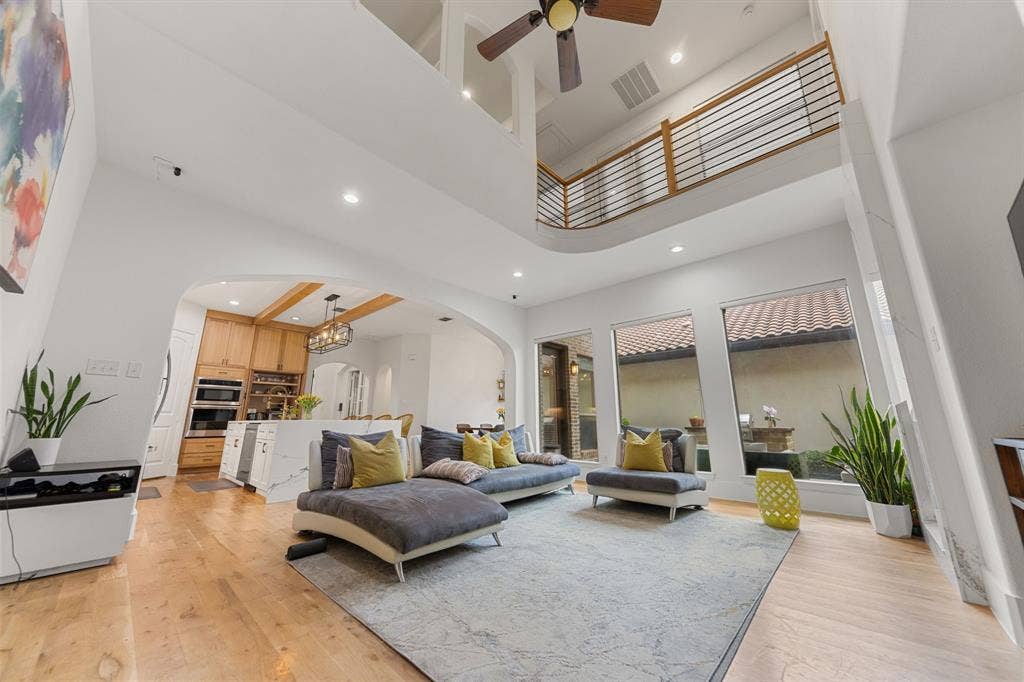 7011 Nueces Drive, Irving, TX 75039 Double-height ceiling with recessed lighting, wood-finish flooring, arched entryway to the kitchen, a curved balcony with metal railings, and multiple windows