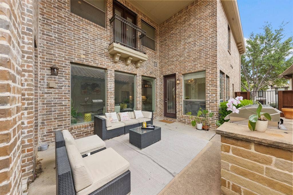 7011 Nueces Drive, Irving, TX 75039 Private outdoor patio with brick exterior, large windows, and an upper-level balcony with iron railing