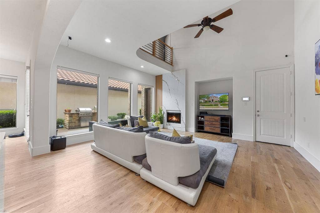 7011 Nueces Drive, Irving, TX 75039 Vaulted ceiling with a ceiling fan, fireplace with a stone-finish facade, wood-finish flooring, built-in media niche, and an exterior patio with a built-in grill