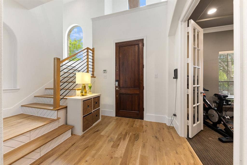 7011 Nueces Drive, Irving, TX 75039 Light wood-finish flooring, dark wood entry door, staircase with wood treads and metal balusters, arched window, and French doors with glass panels