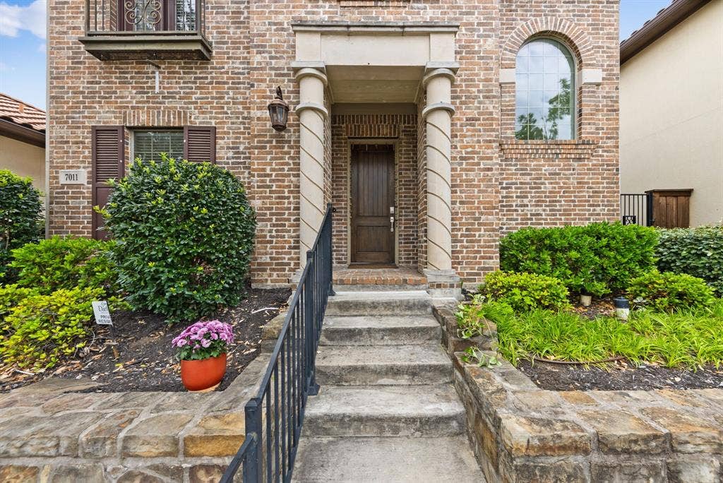 7011 Nueces Drive, Irving, TX 75039 Brick exterior with stone accents, arched window, wrought iron railing, and mature landscaping