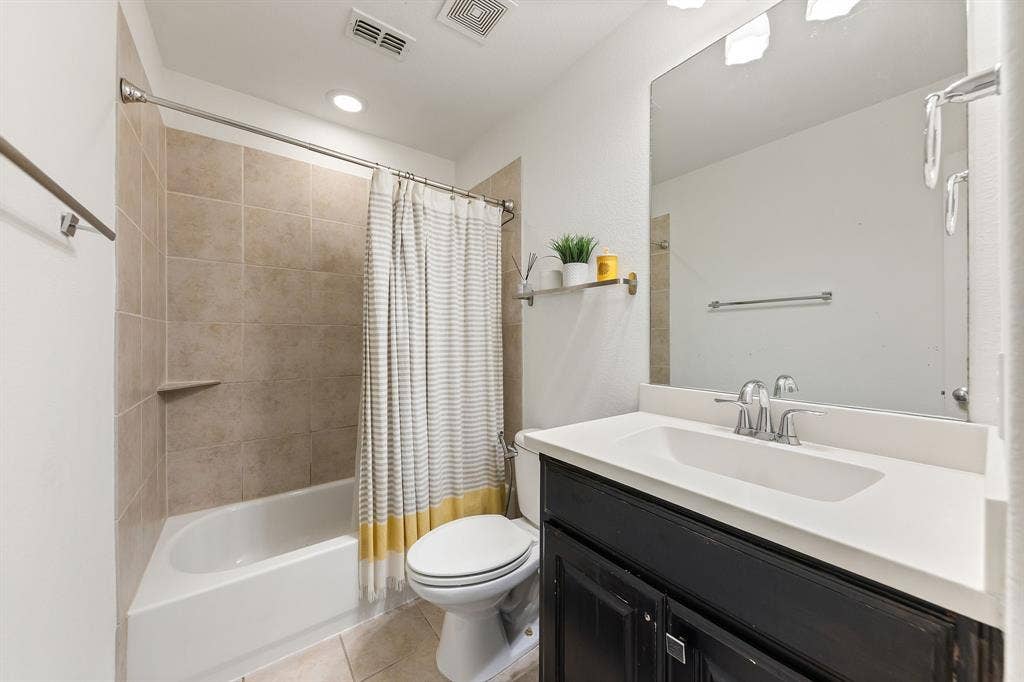 7011 Nueces Drive, Irving, TX 75039 White bathtub with tiled surround, recessed lighting, and a dark wood vanity with white countertop