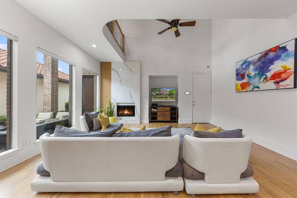 7011 Nueces Drive, Irving, TX 75039 Vaulted ceiling living area with wood-finish flooring, a contemporary fireplace with a large stone surround, and expansive windows