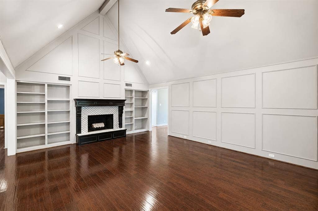 Vaulted ceiling with wood-finish flooring, featuring a fireplace with tile surround, built-in shelving, and decorative wall paneling
