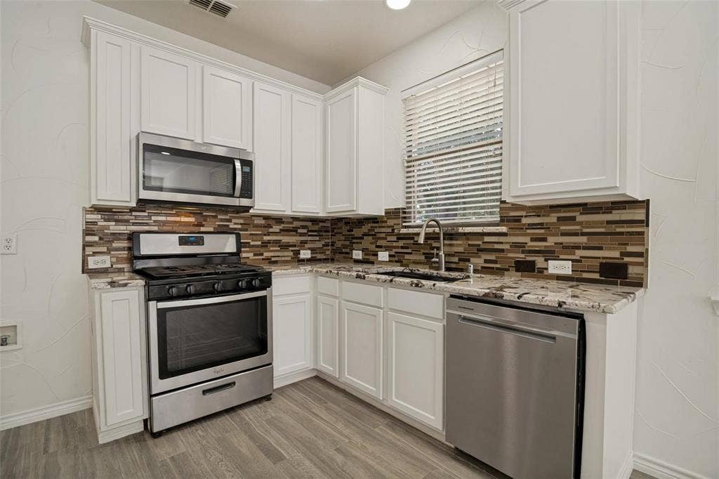 1516 Cedar Grove Court, Allen, TX 75002 Kitchen featuring white cabinetry, stainless steel appliances, granite-style countertops, mosaic tile backsplash, and wood-finish flooring