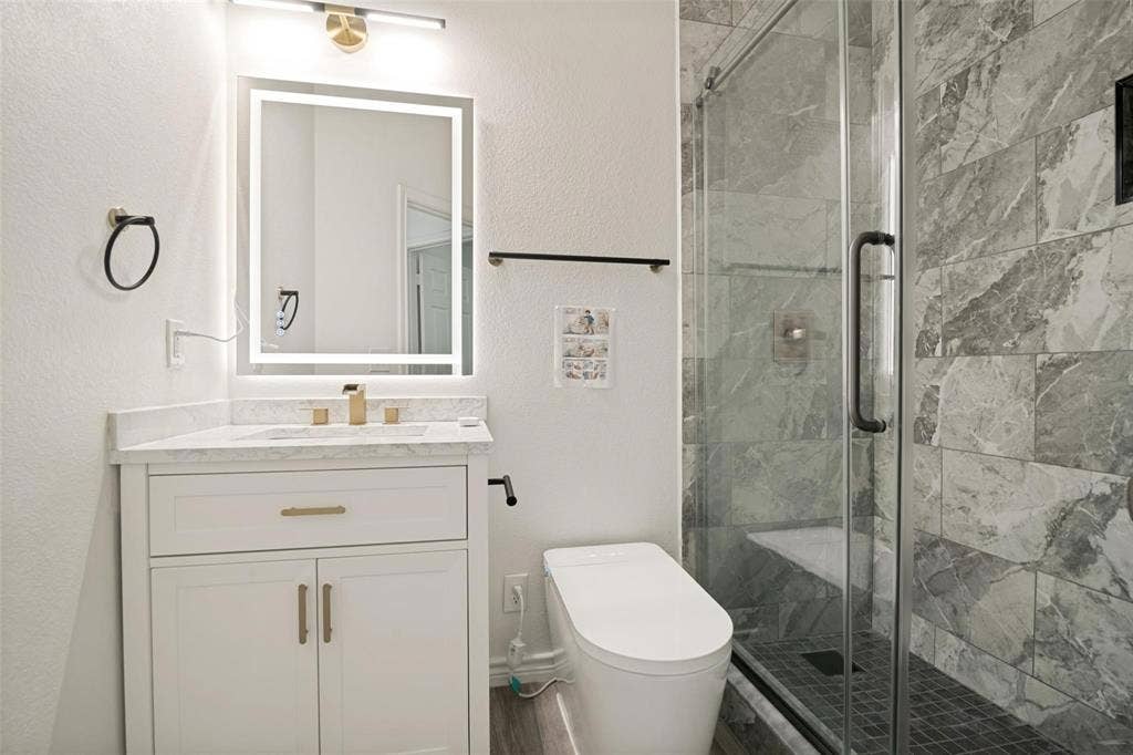 1516 Cedar Grove Court, Allen, TX 75002 Walk-in shower with tiled walls and glass enclosure, floating vanity with a stone countertop, illuminated mirror, and modern toilet