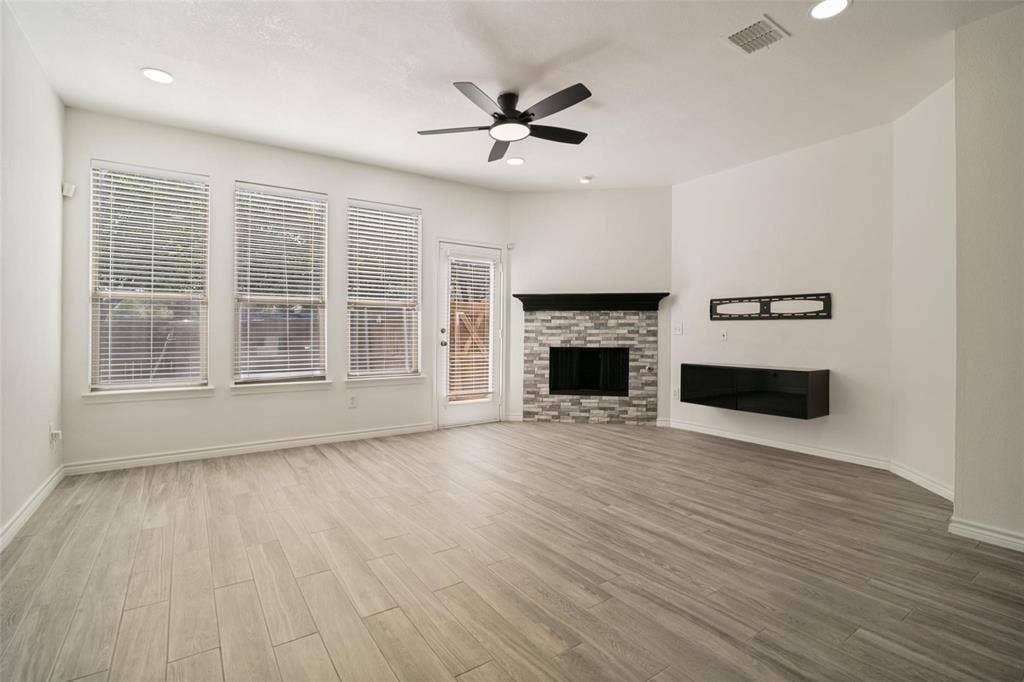 1516 Cedar Grove Court, Allen, TX 75002 Spacious living area featuring wood-finish flooring, a stacked stone fireplace with a dark mantel, multiple windows, a ceiling fan, and recessed lighting