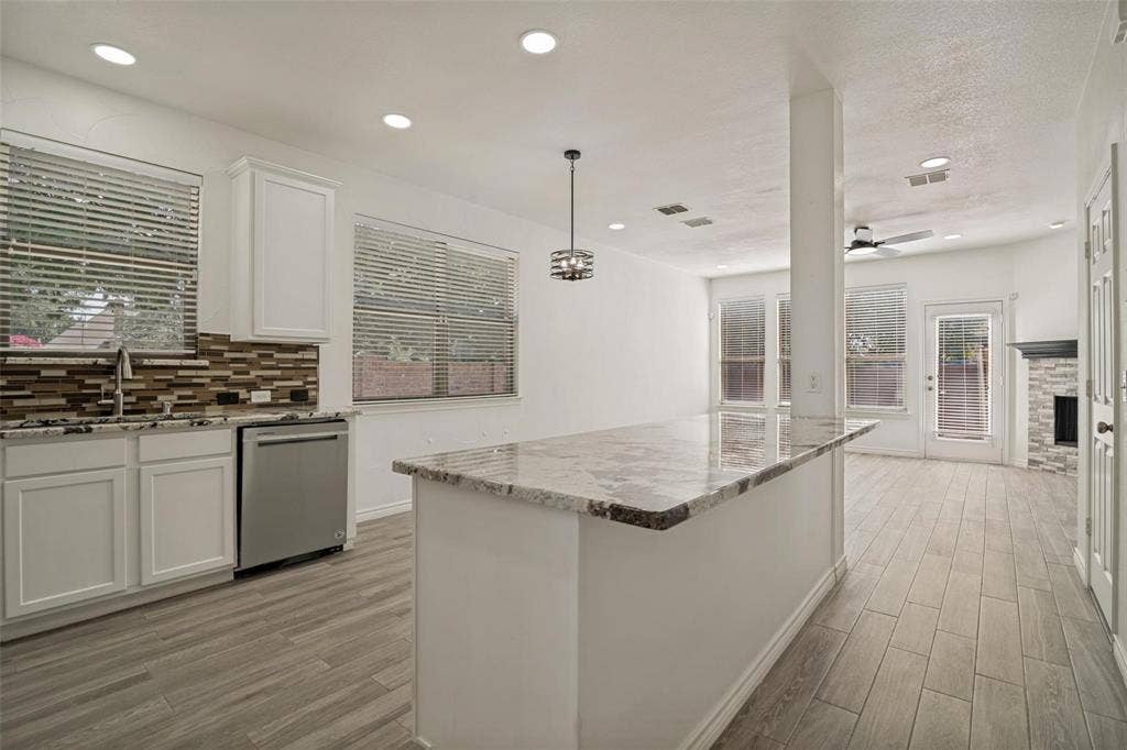 1516 Cedar Grove Court, Allen, TX 75002 Kitchen with wood-finish flooring, white cabinetry, a large center island with a light-colored countertop, and a mosaic tile backsplash