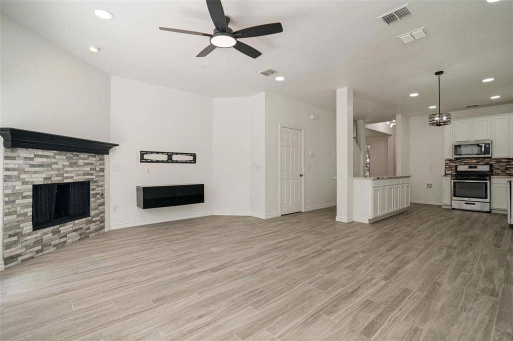 1516 Cedar Grove Court, Allen, TX 75002 Spacious living area featuring wood-finish tile flooring, a fireplace with a stone surround and dark wood mantel, and a ceiling fan